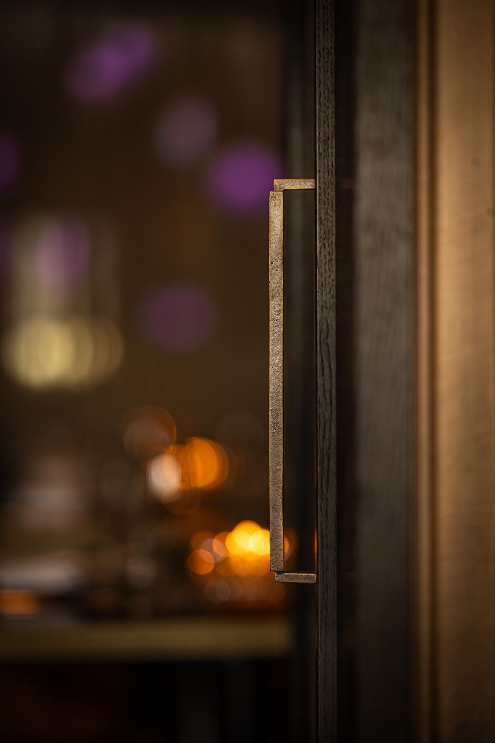 Close-up of a dark wooden cabinet door handle with warm blurred lights in the background