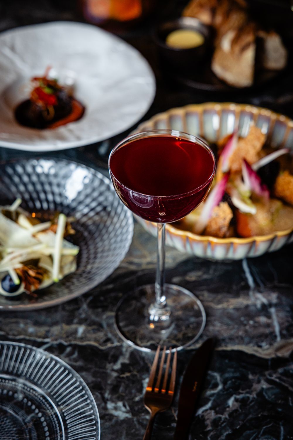 Elegant table setting with a red cocktail, plated dishes, and a dark marble tabletop