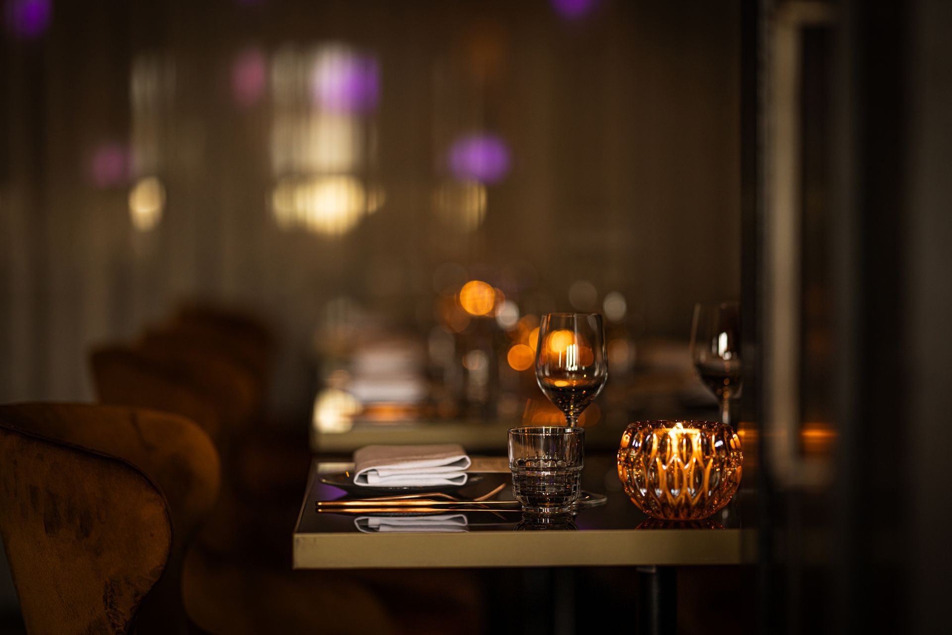 Dimly lit restaurant table set with glassware, candlelight, and menus in a warm, elegant interior