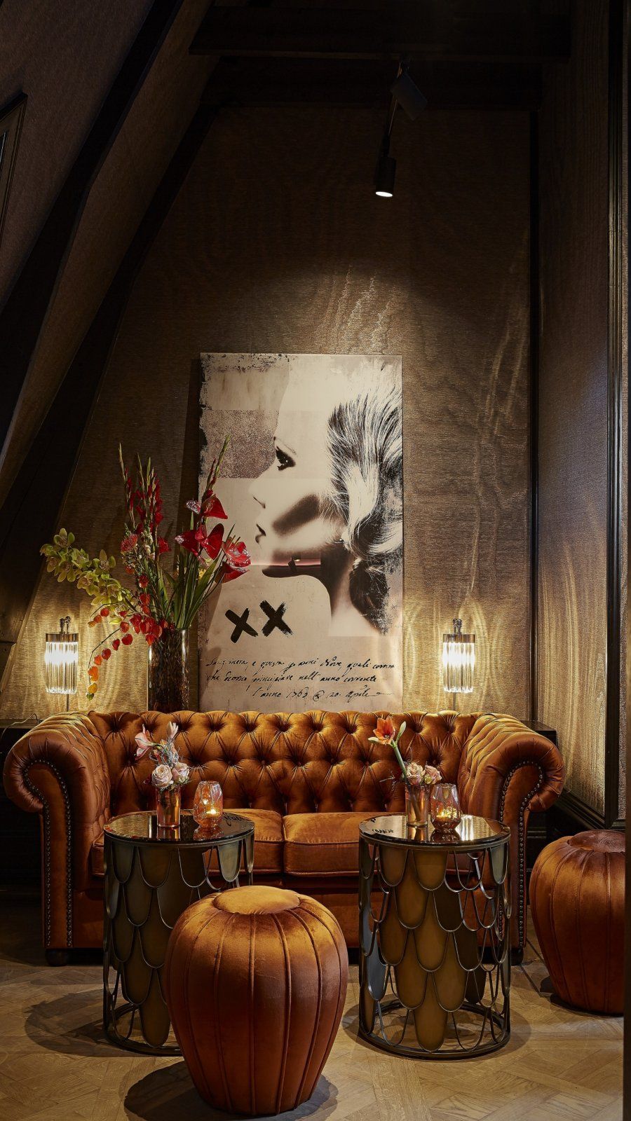 Cozy lounge with a tan leather sofa, round wooden stools, and a large abstract wall artwork.