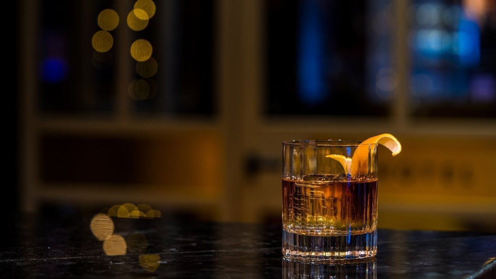 Whiskey glass with ice and an orange peel garnish on a dark bar counter