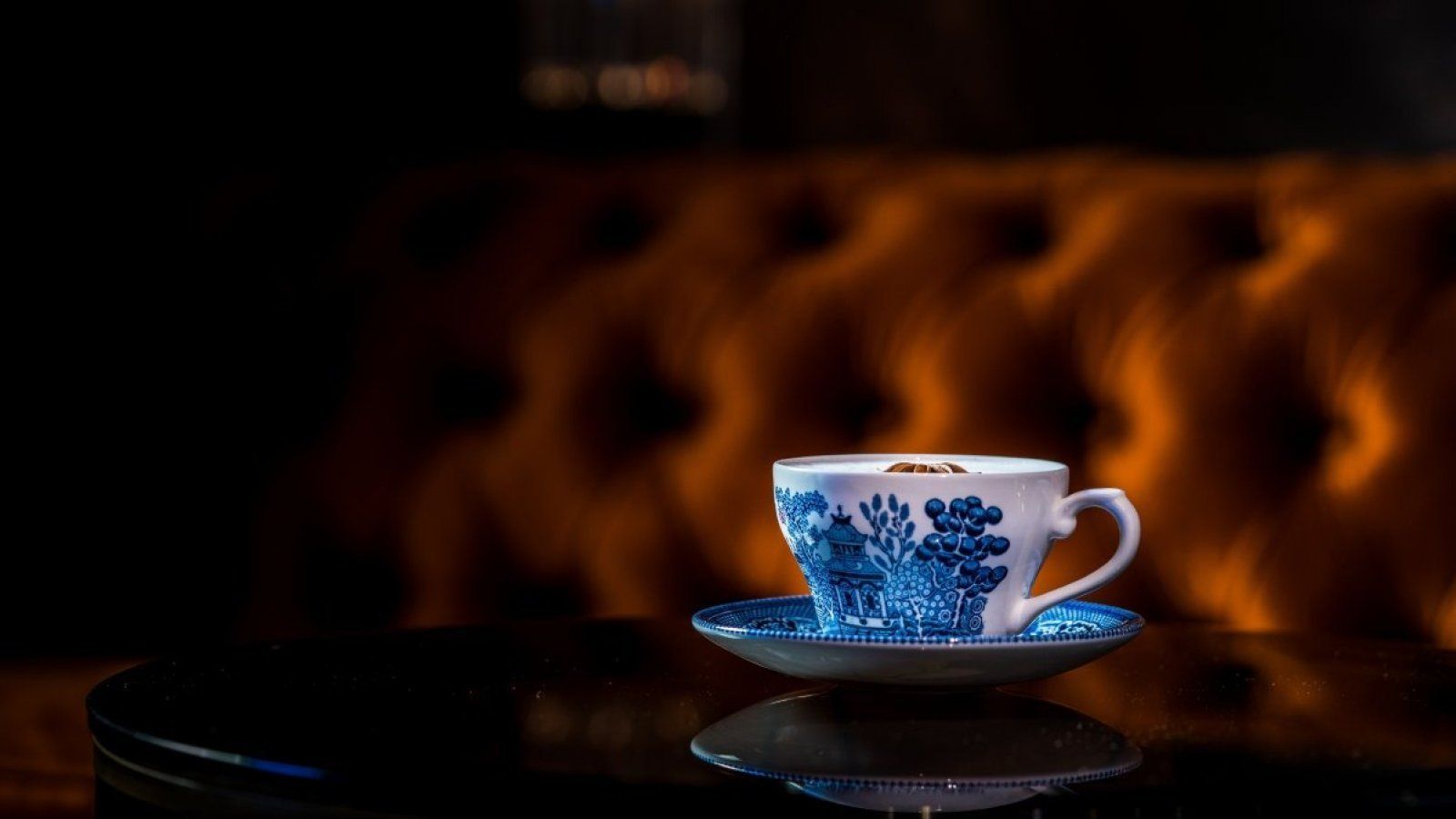 White and blue teacup on saucer against a blurred brown tufted background