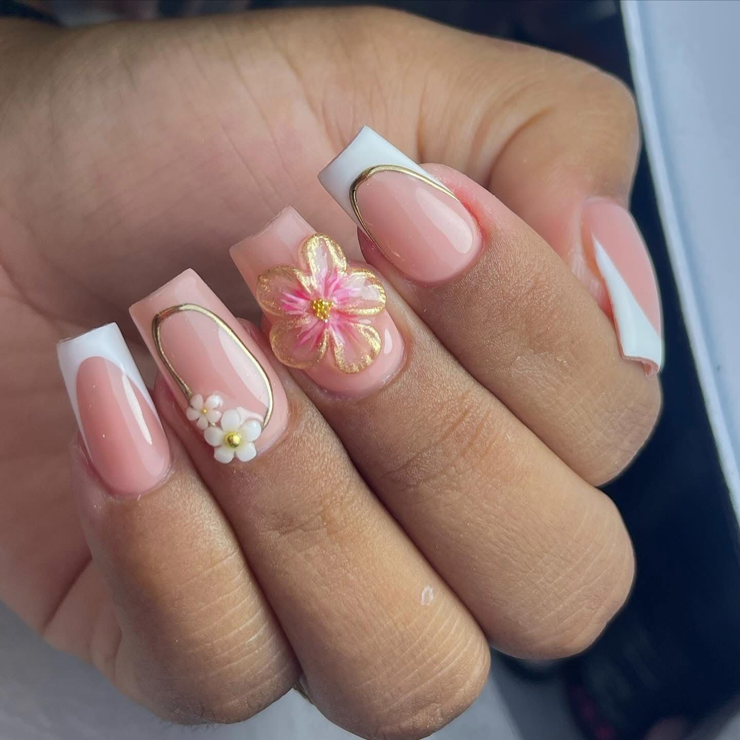 Mano con uñas rosas con punta francesa, contornos dorados y diseño floral en 3D.