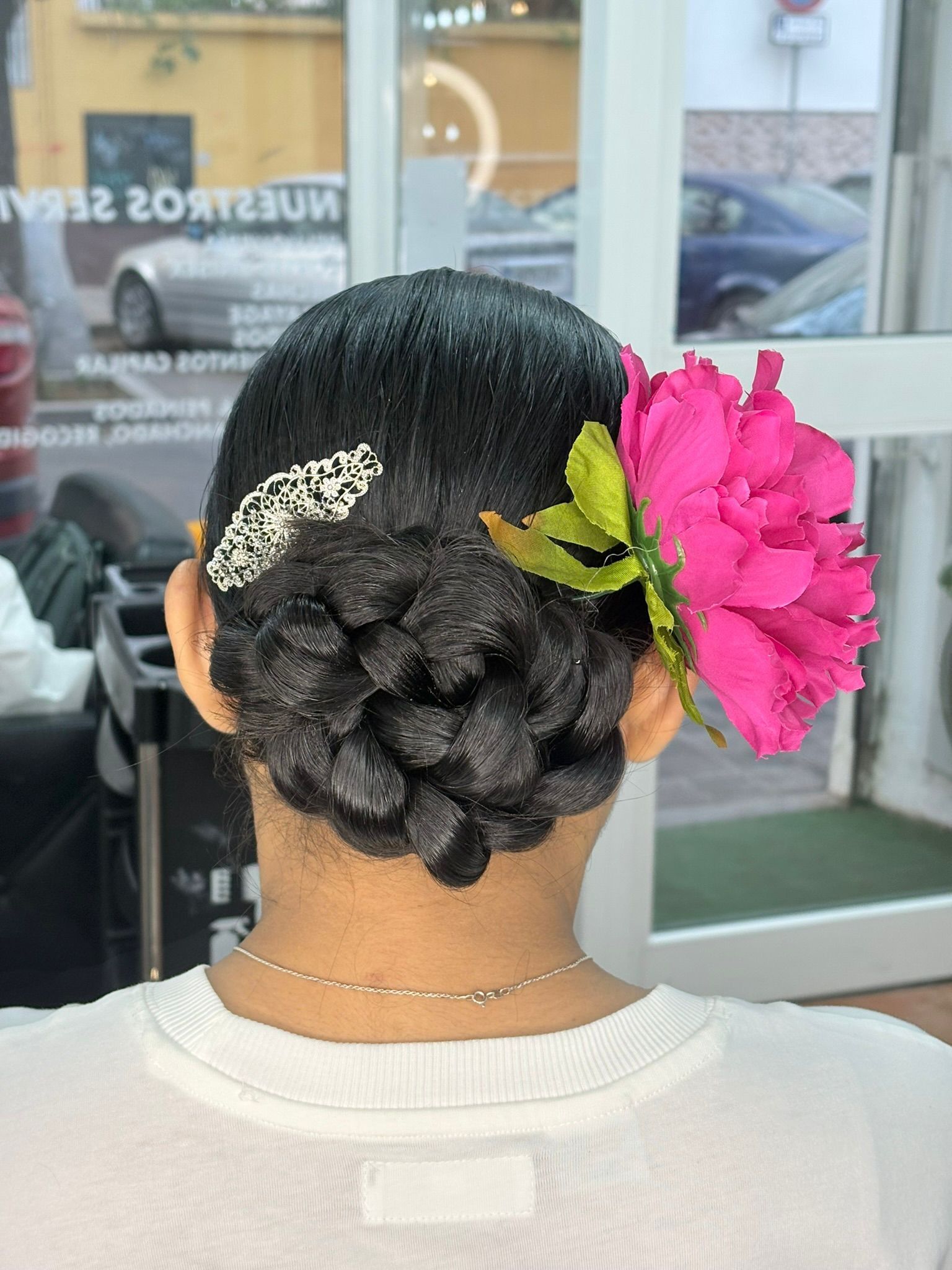 Mujer con un elegante recogido trenzado, una pinza plateada para el cabello y una gran flor rosa