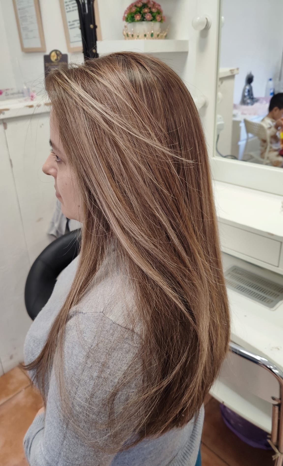 Vista lateral de una persona con cabello largo y con mechas sentada en una silla de peluquería.