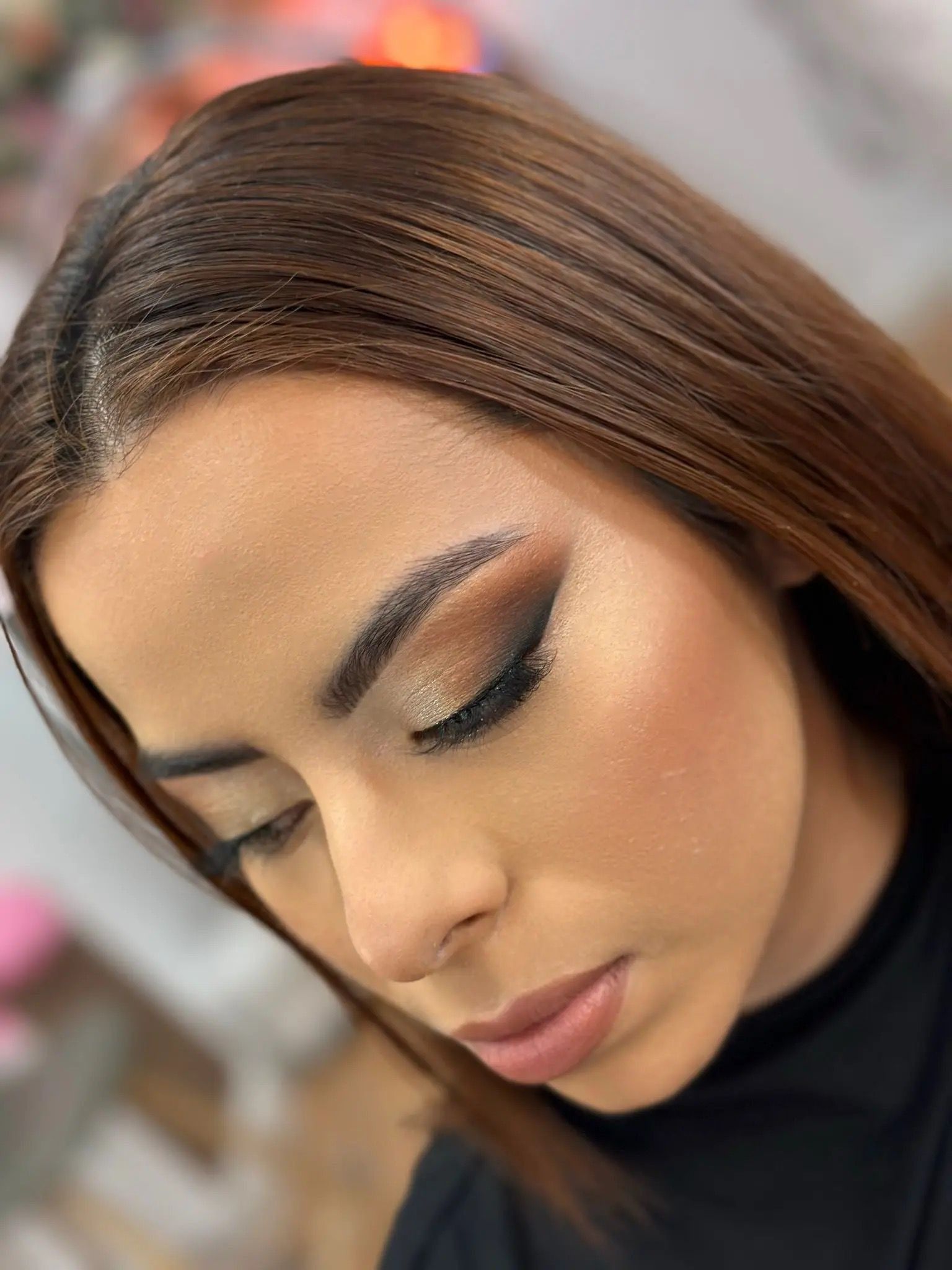 Primer plano de una mujer con cabello castaño liso, maquillaje suave y sombra de ojos brillante, mirando hacia abajo.
