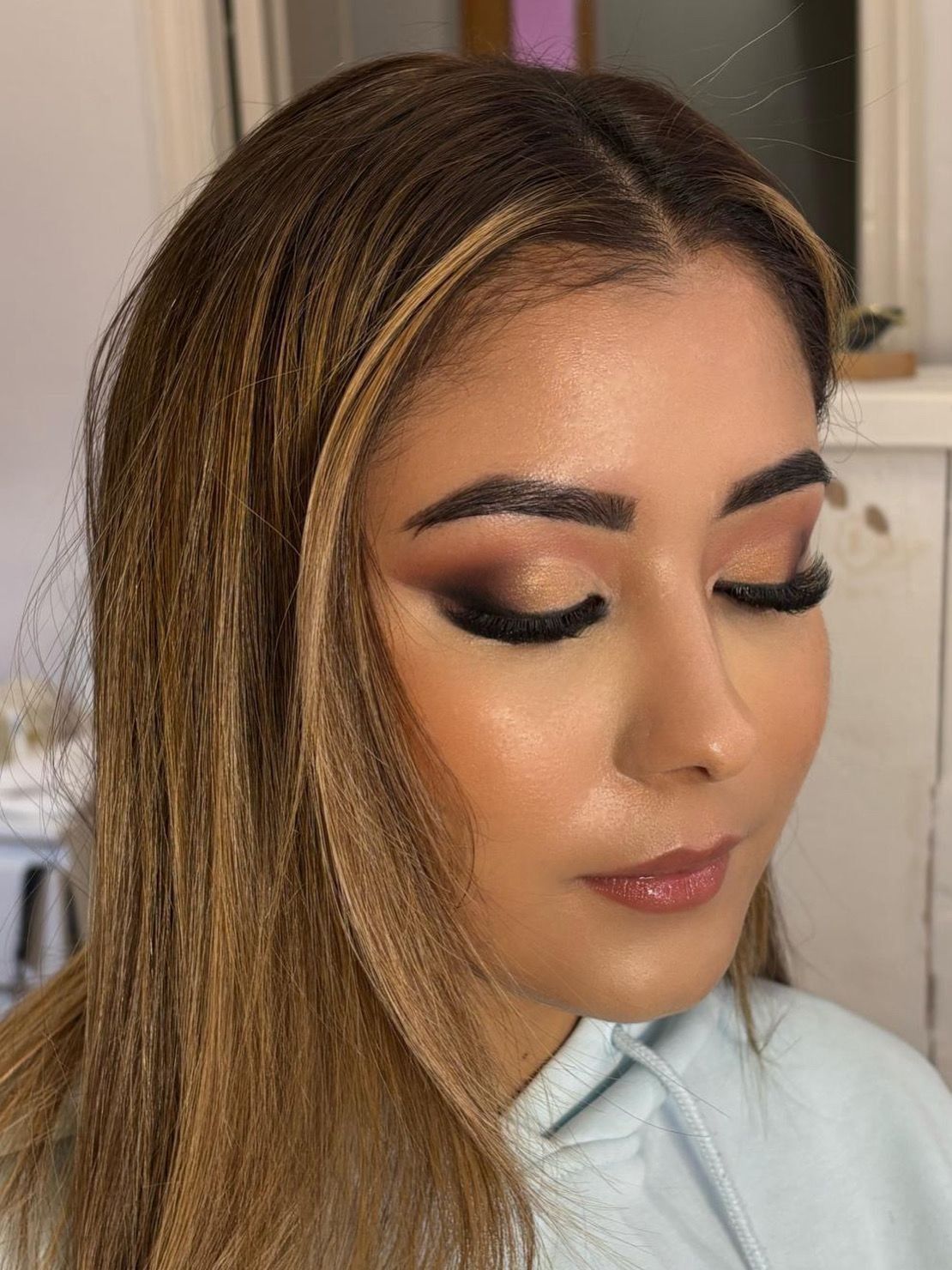 Mujer con cabello largo con mechas y maquillaje suave y glamuroso, mirando hacia abajo