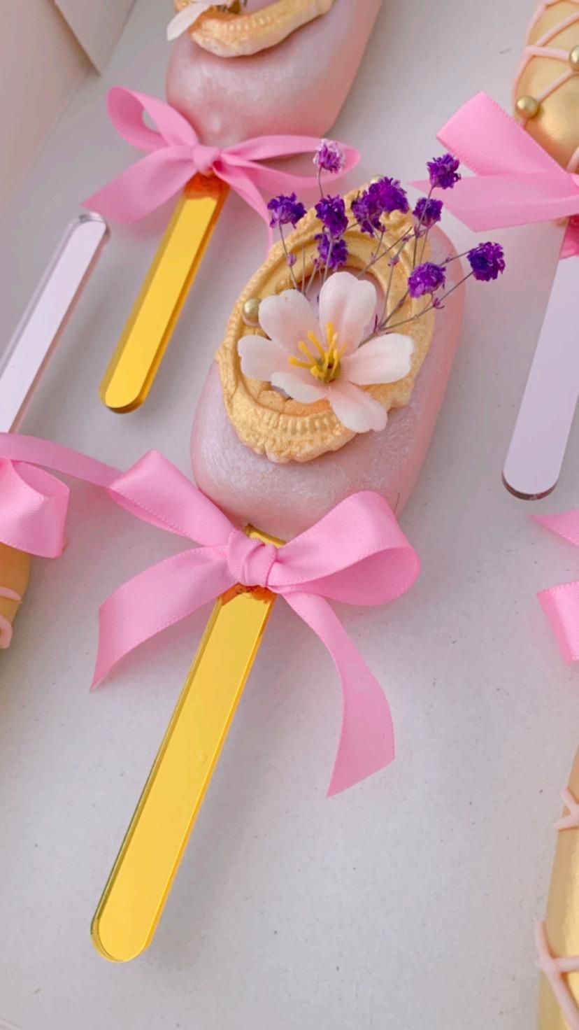 Un primer plano de un cake pop rosa y dorado con flores y un lazo.