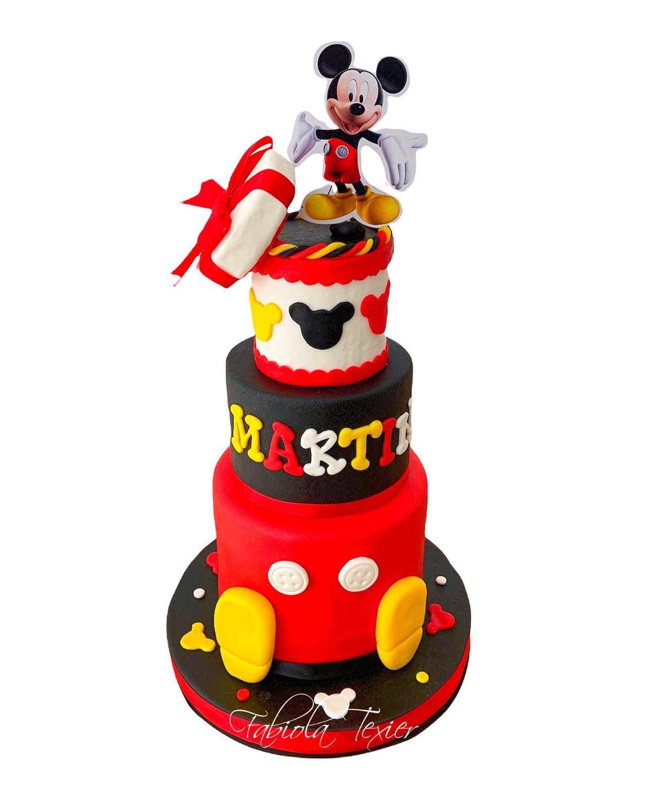 Un pastel de Mickey Mouse de tres niveles con una figura de Mickey Mouse en la parte superior.