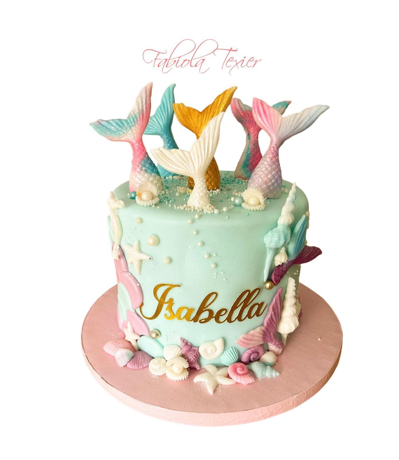 Un pastel con decoraciones de cola de sirena y el nombre Isabella en él.