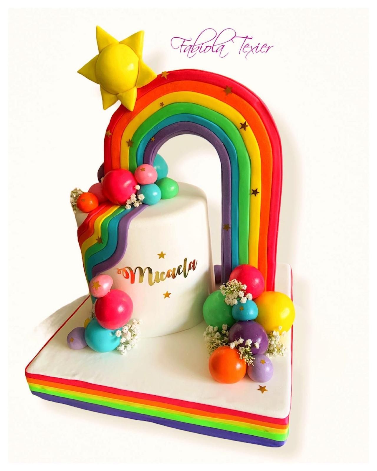 Un pastel con un arcoíris y globos encima.