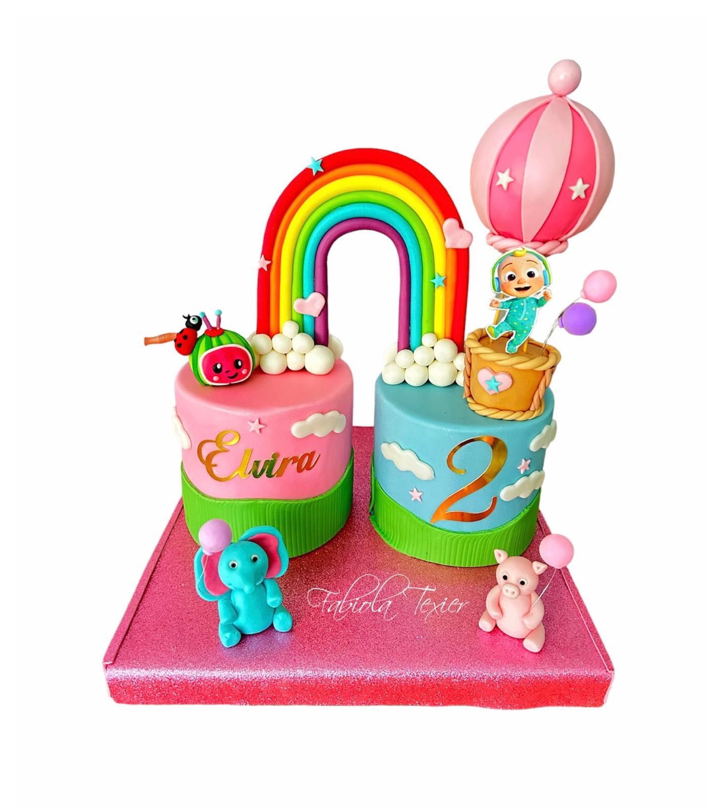 Un pastel de cumpleaños para una niña con un arcoíris y globos aerostáticos.