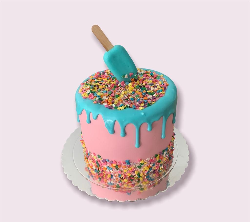 Un pastel rosa y azul con chispas y una paleta encima.
