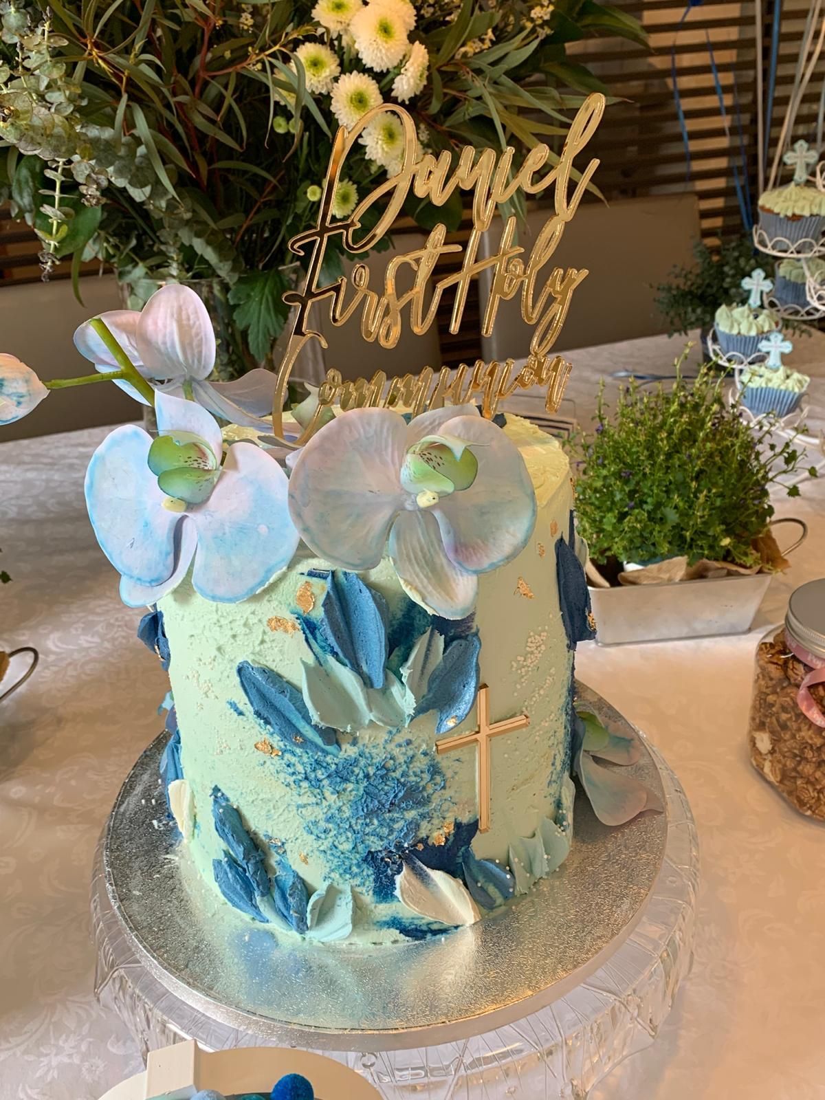 Sobre una mesa hay un pastel con flores y una cruz encima.