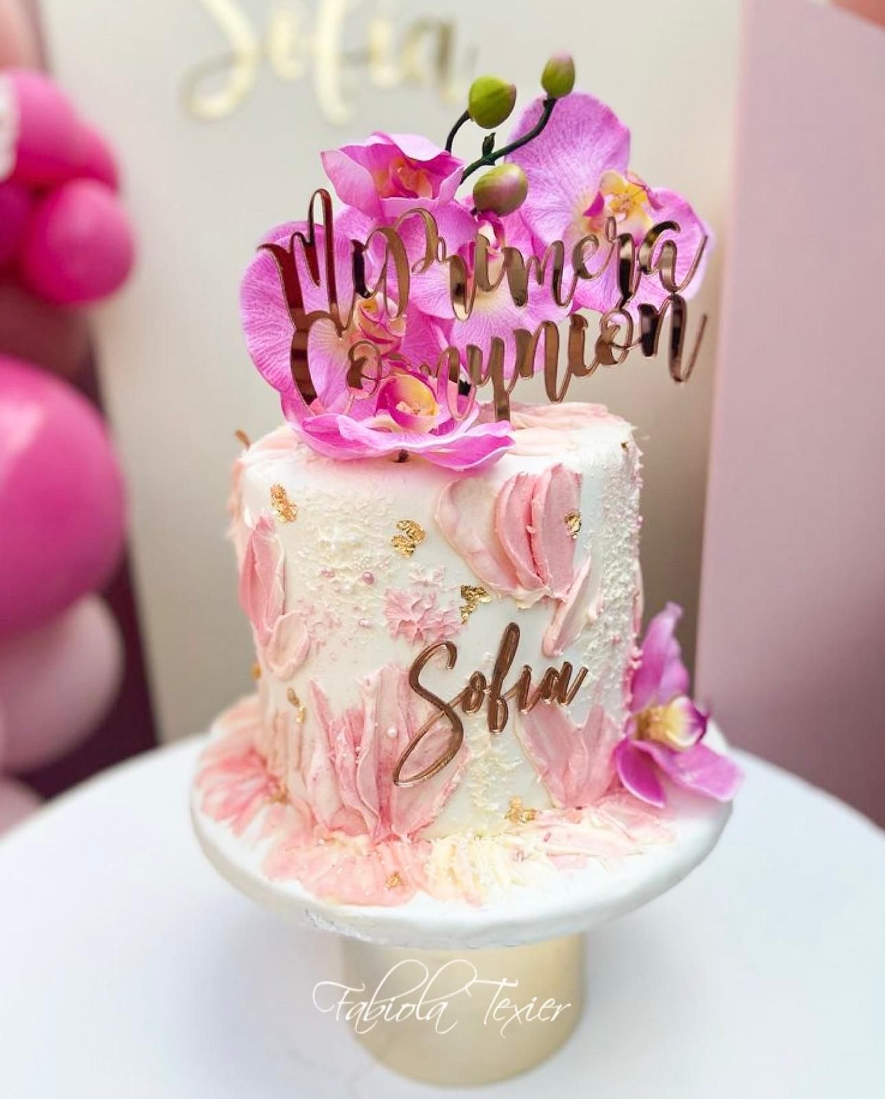 Un pastel con flores rosas y un nombre está sobre una mesa.