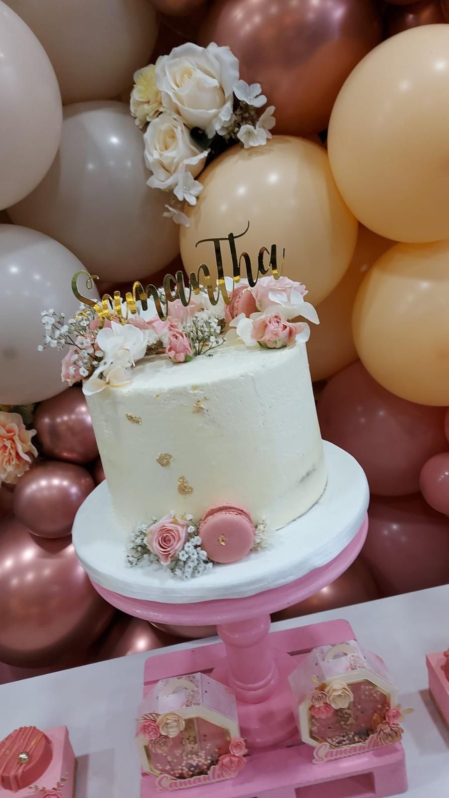 Un pastel está colocado encima de un soporte para pasteles de color rosa delante de globos.