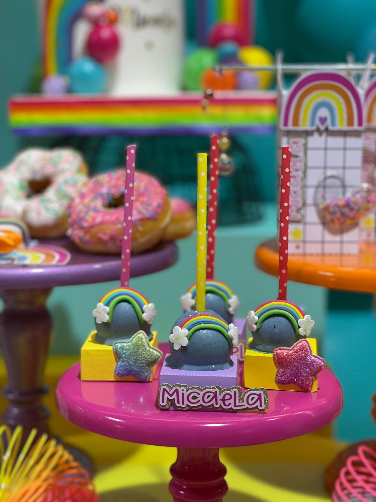 Una mesa cubierta con un montón de cake pops con arcoíris sobre ellos.