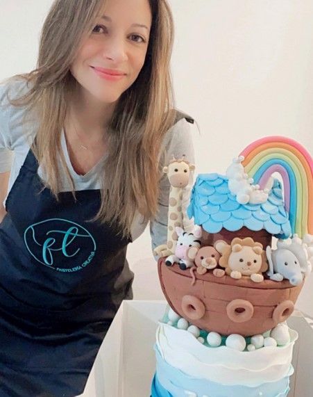 Una mujer con un delantal está de pie junto a un pastel del arca de Noé.