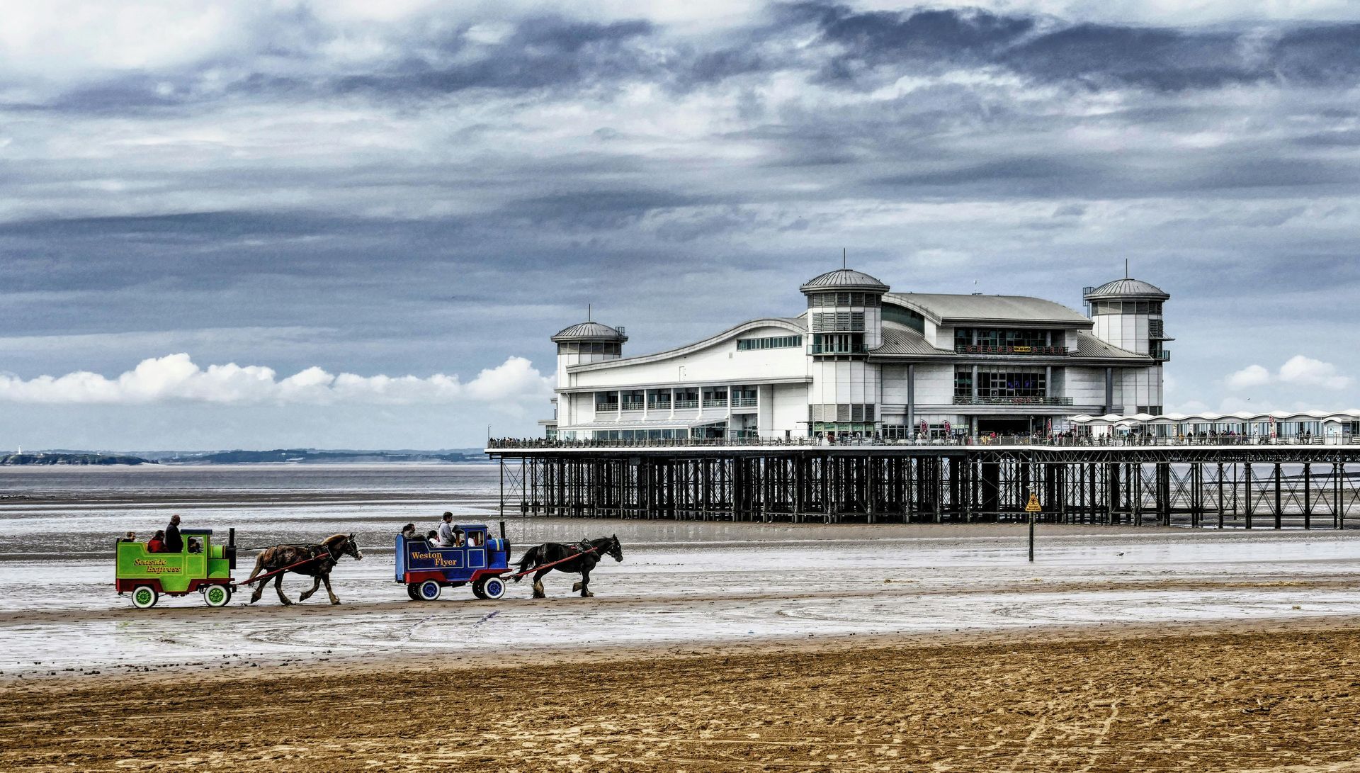 A horse drawn carriage on a beach with a pier in the background in Weston super Mare.