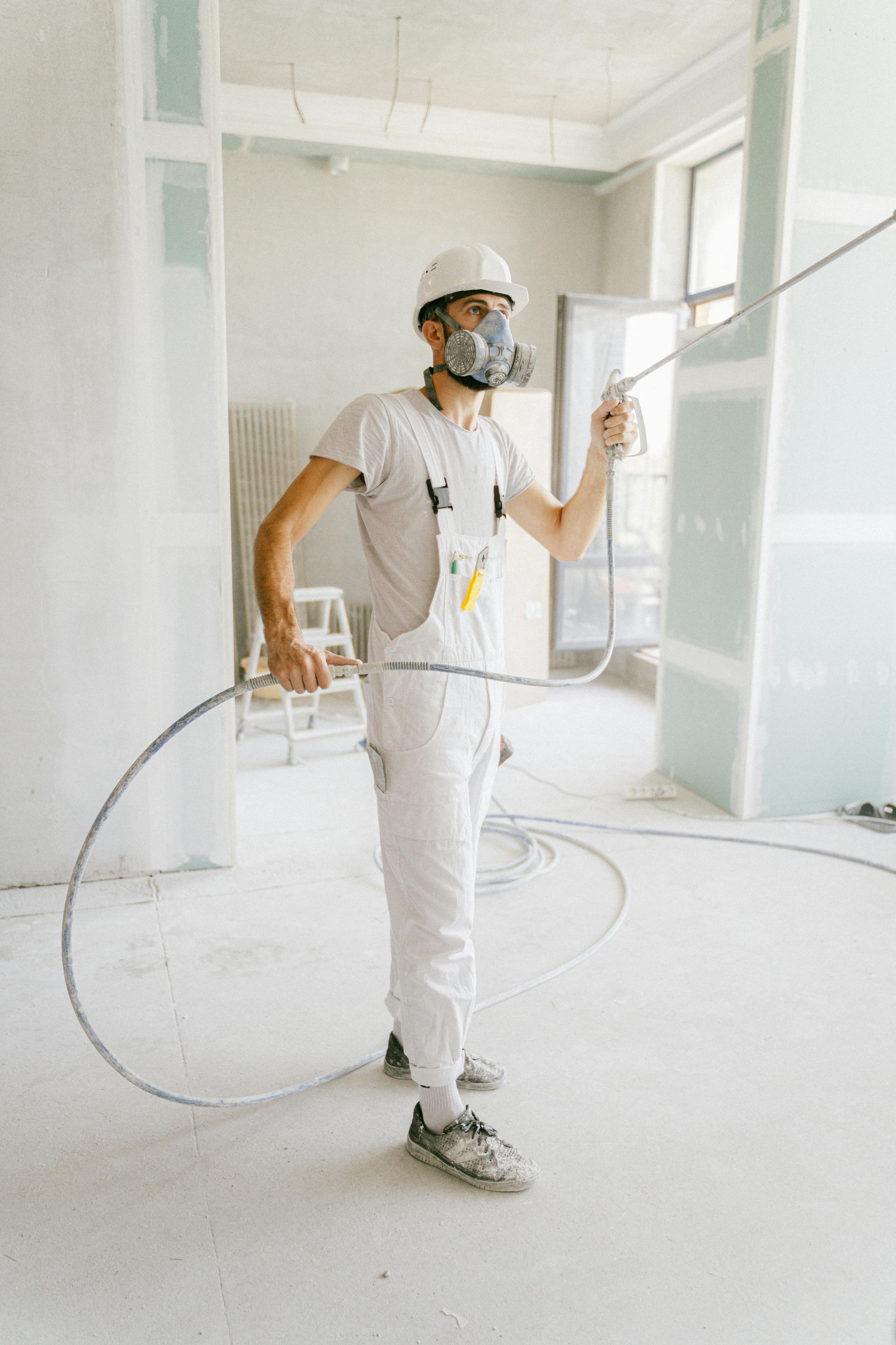 A man wearing a mask is painting a wall with a sprayer.