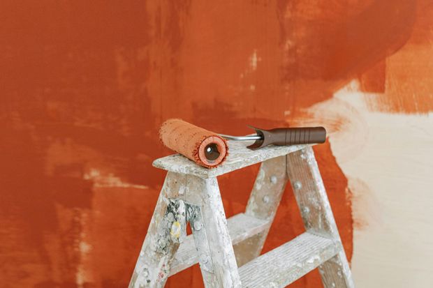 A paint roller is sitting on top of a wooden ladder.