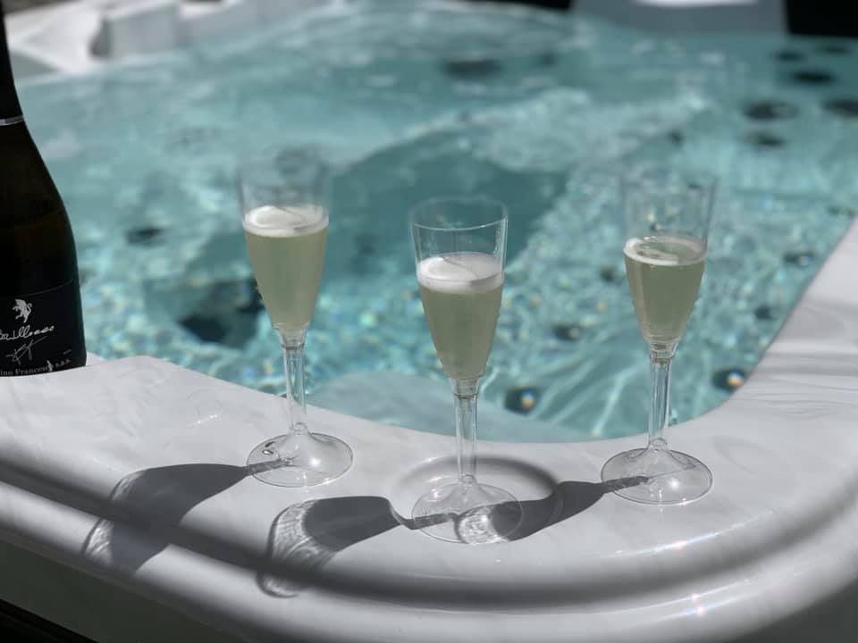 Trois verres de champagne et une bouteille reposent sur le bord d'un jacuzzi.