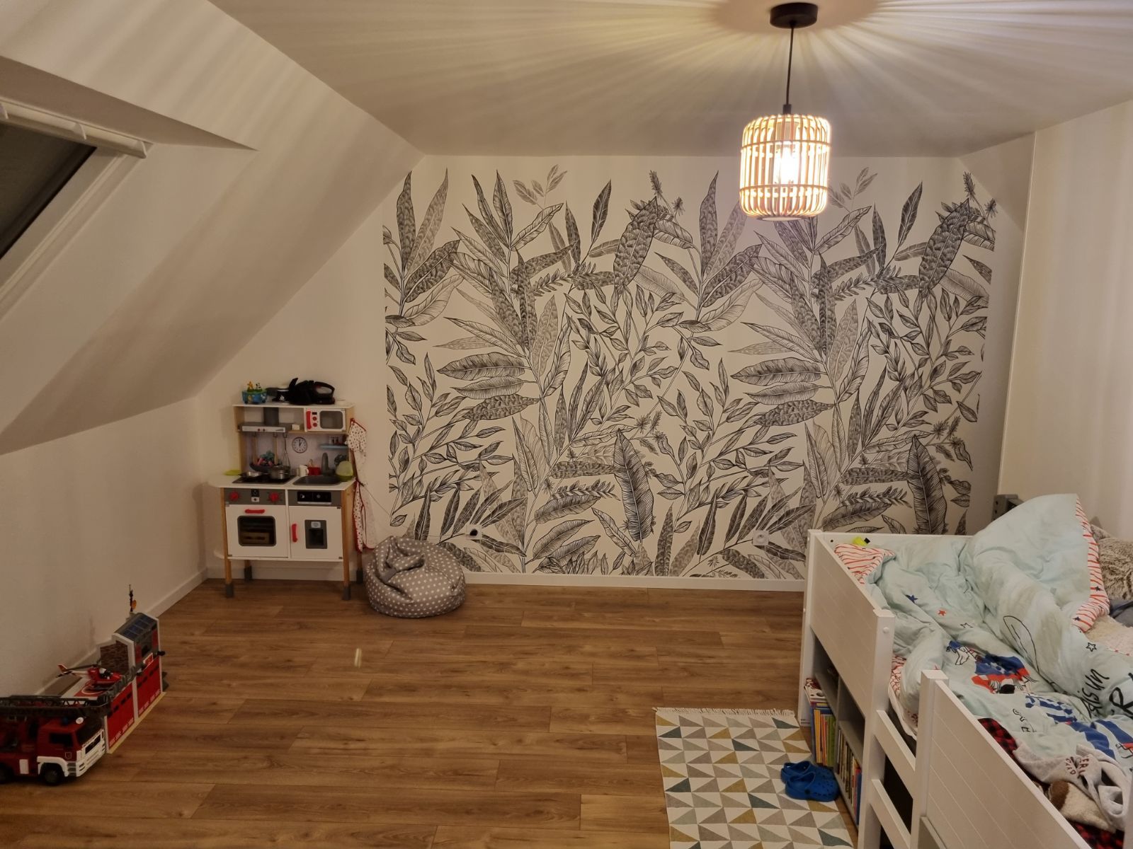Chambre d'enfant avec un mur d'accent orné de papier peint botanique, parquet, cuisine de jeu et lit superposé.