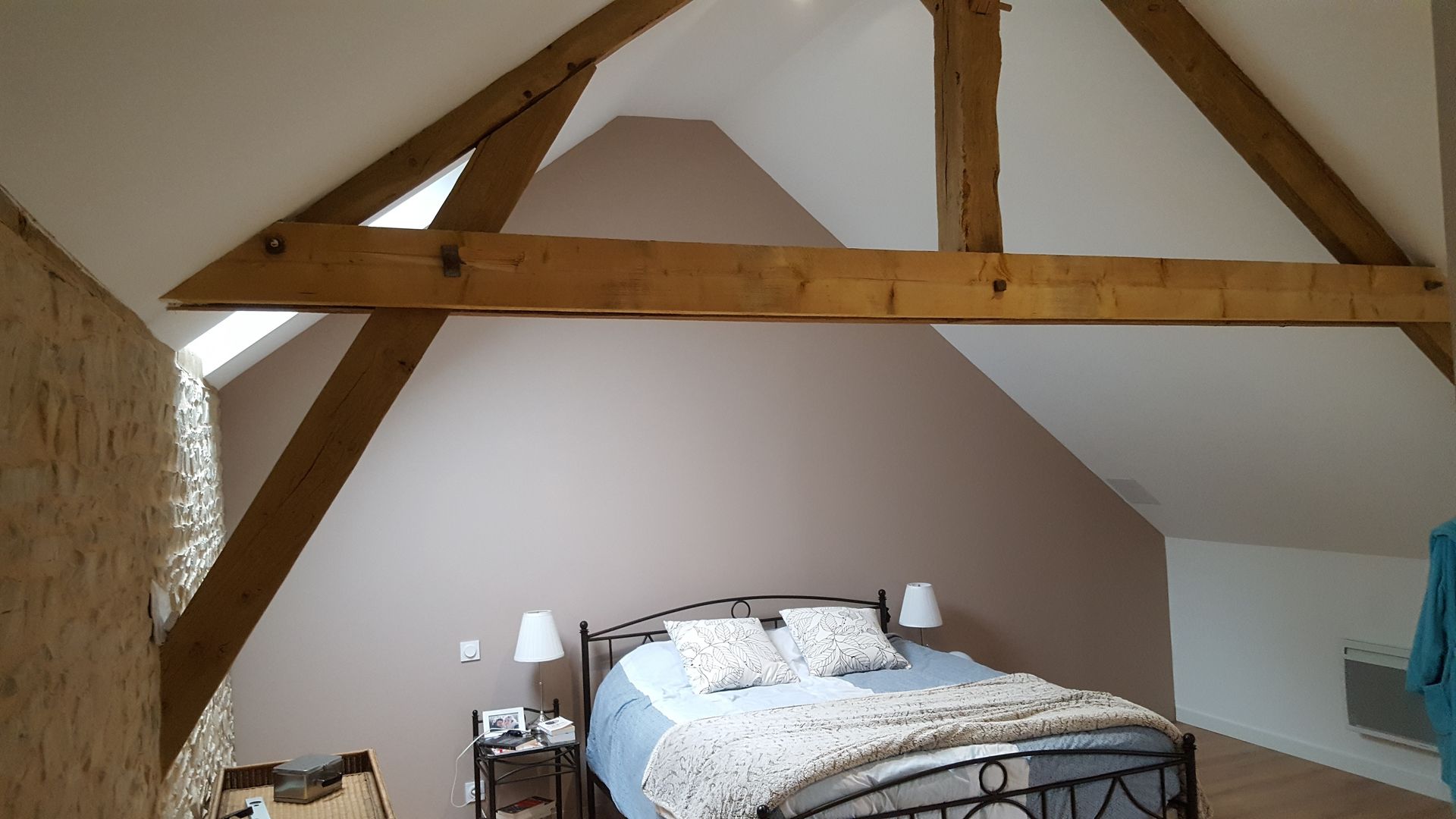 Chambre avec poutres apparentes, murs rose pâle et lit avec draps bleus.