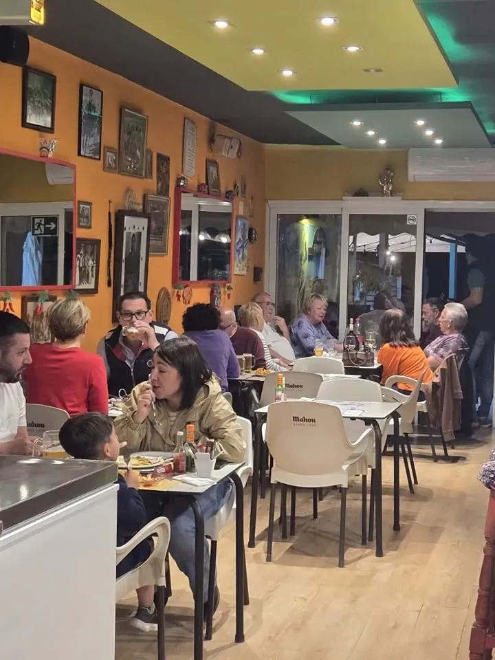 Cafetería moderna y concurrida con gente comiendo en mesas bajo una cálida iluminación naranja.