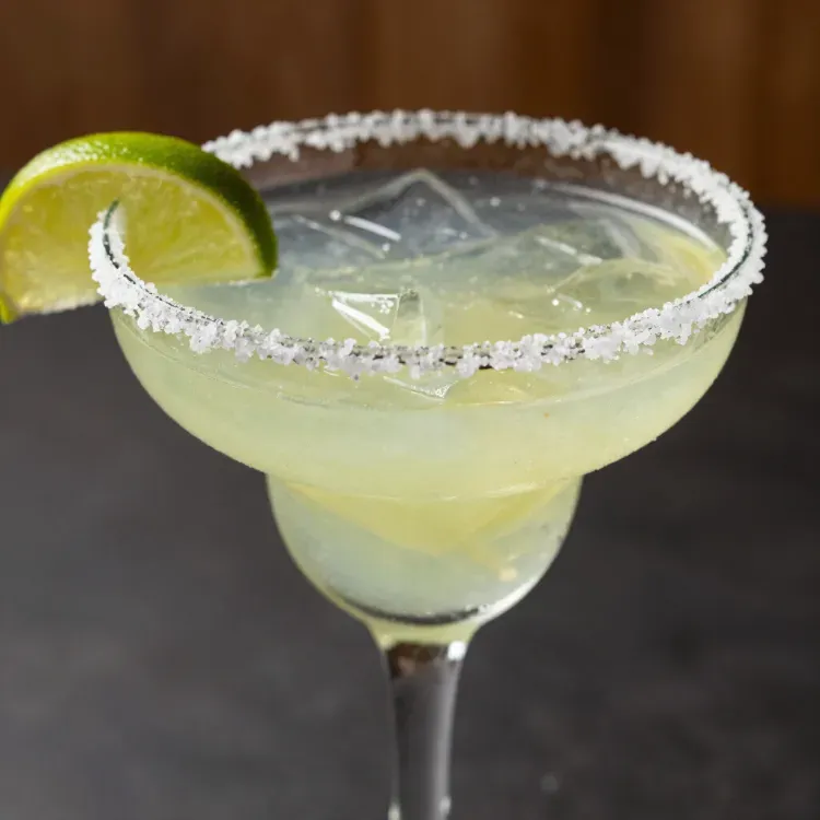 Cóctel Margarita con borde salado y rodaja de lima en una copa con tallo.