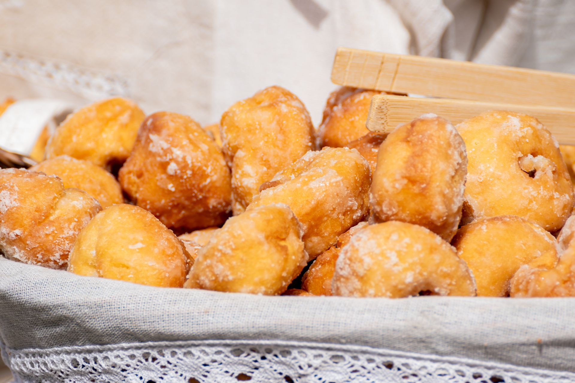 Panier de beignets sucrés, dorés, dans un panier de couleur claire avec des pinces.