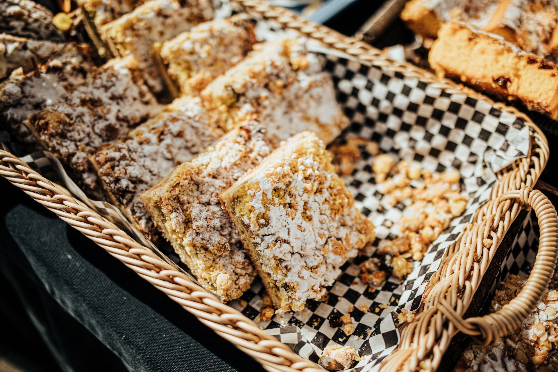 Panier de carrés friables cuits au four, certains saupoudrés de sucre glace, dans un panier tressé avec doublure à carreaux.