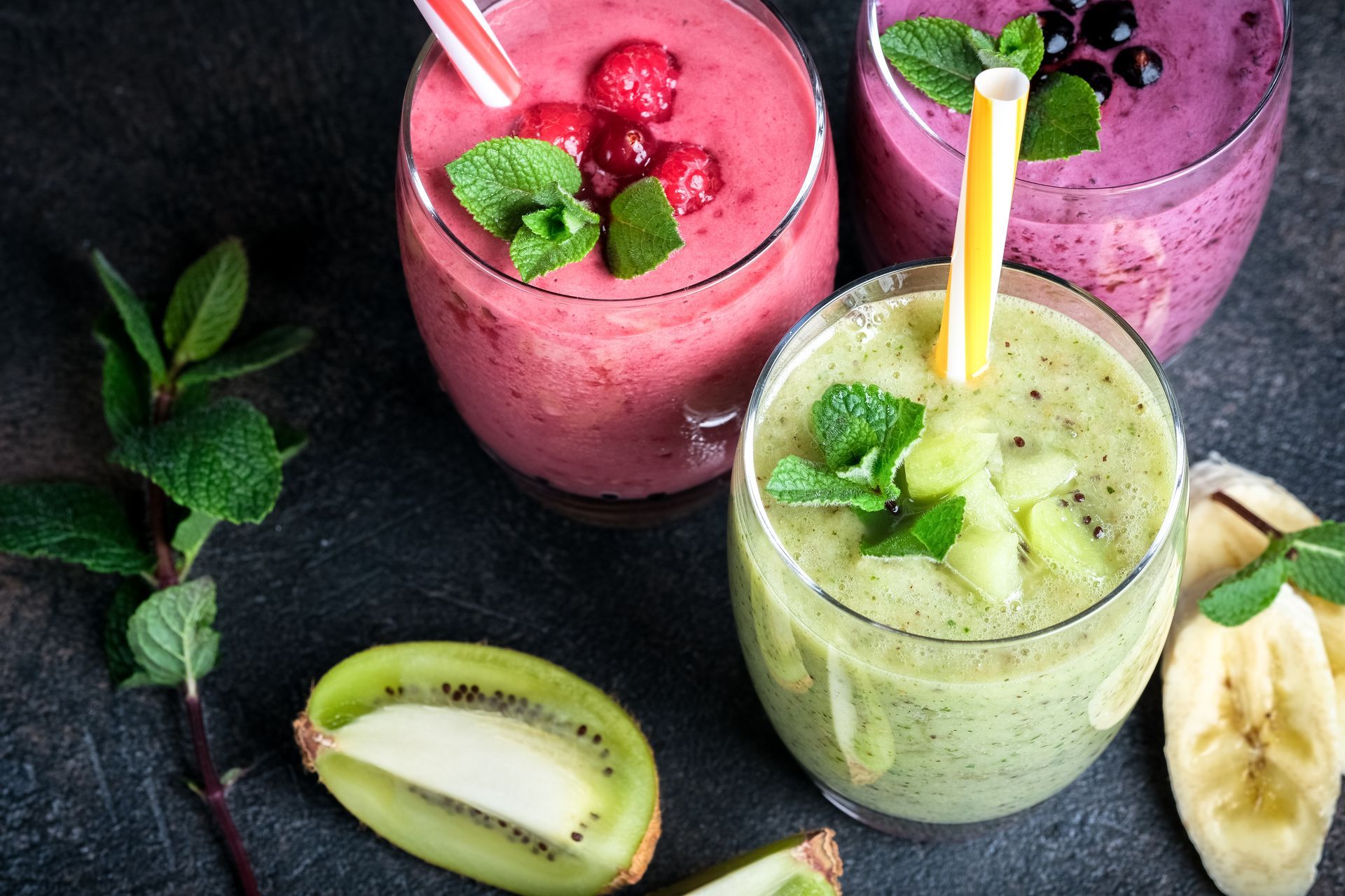 Trois smoothies colorés avec des garnitures de fruits et des pailles.