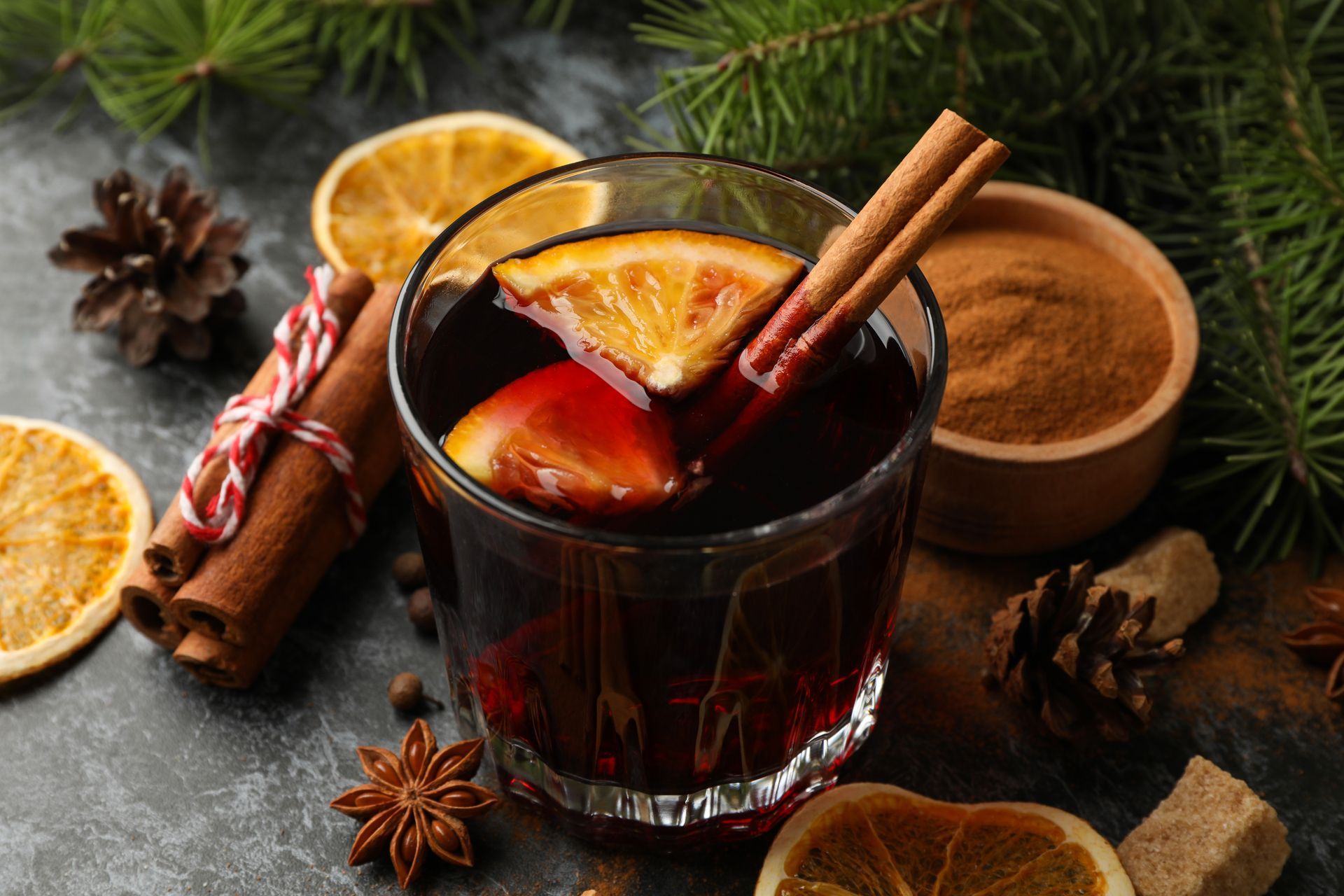 Verre de vin chaud avec tranche d'orange et bâton de cannelle, décorations de fêtes.