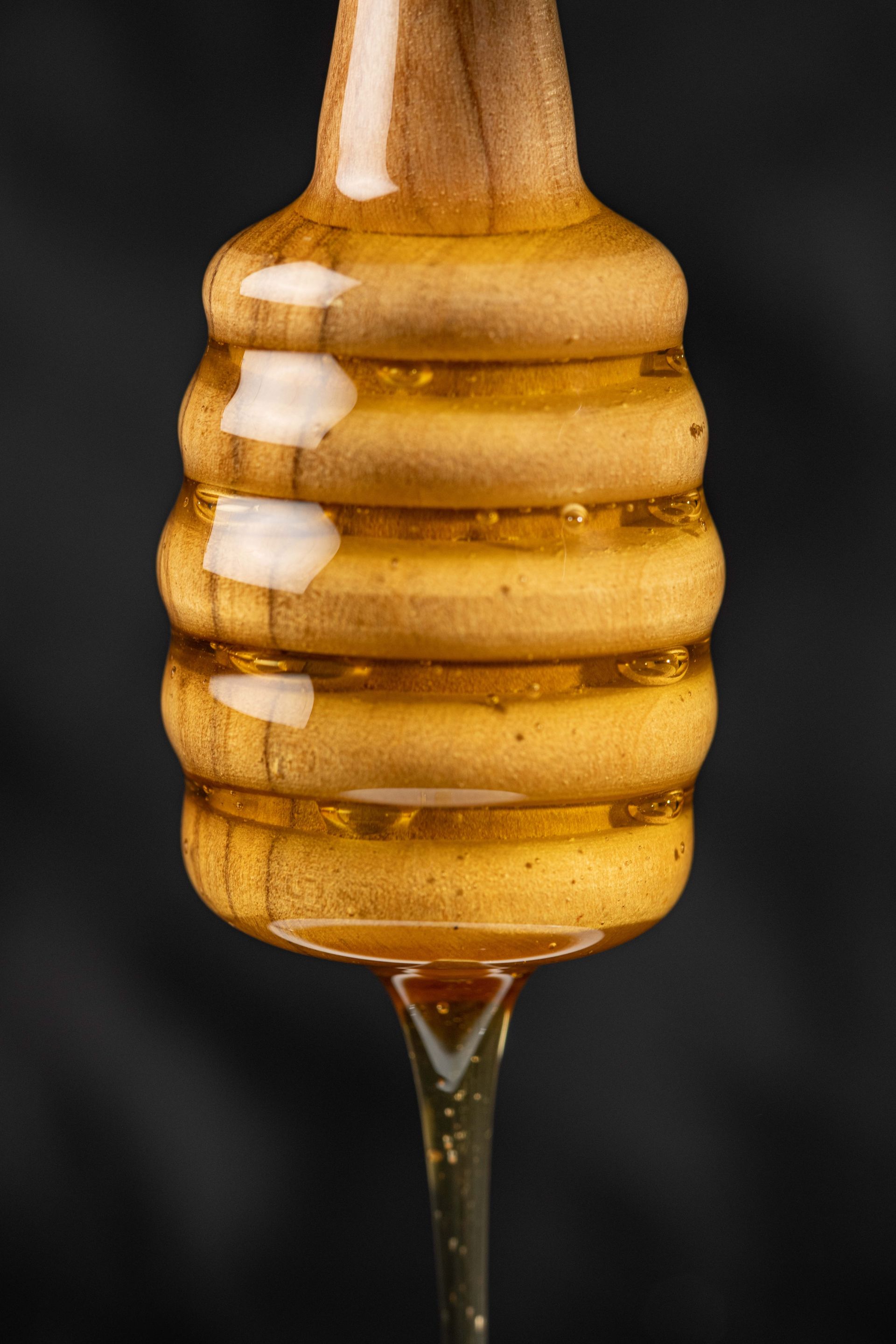 Cuillère à miel dégoulinant de miel doré sur un fond noir.