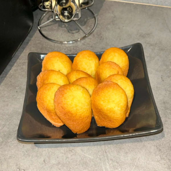 Madeleines dorées sur une assiette carrée noire posée sur un comptoir gris.