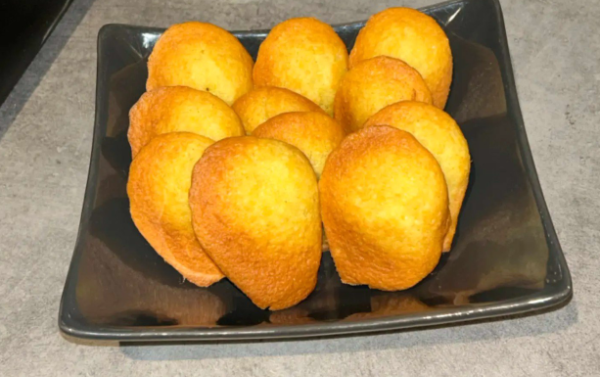 Madeleines dorées disposées sur une assiette carrée foncée, prêtes à être dégustées.