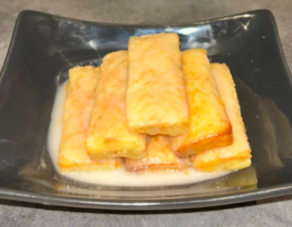 Bâtonnets de pain perdu dans un bol gris, partiellement immergés dans une sauce au lait.