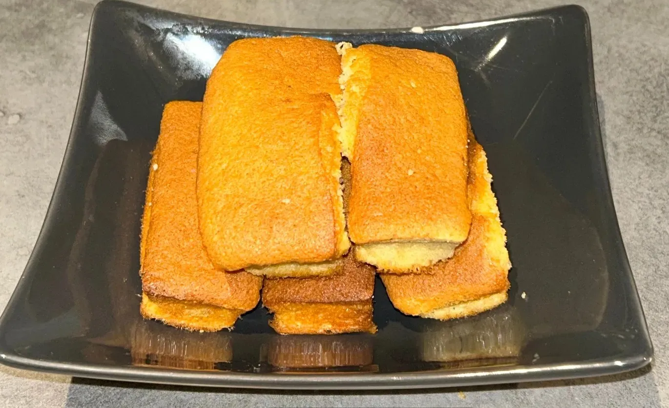 Gâteaux rectangulaires dorés empilés sur une assiette carrée foncée.