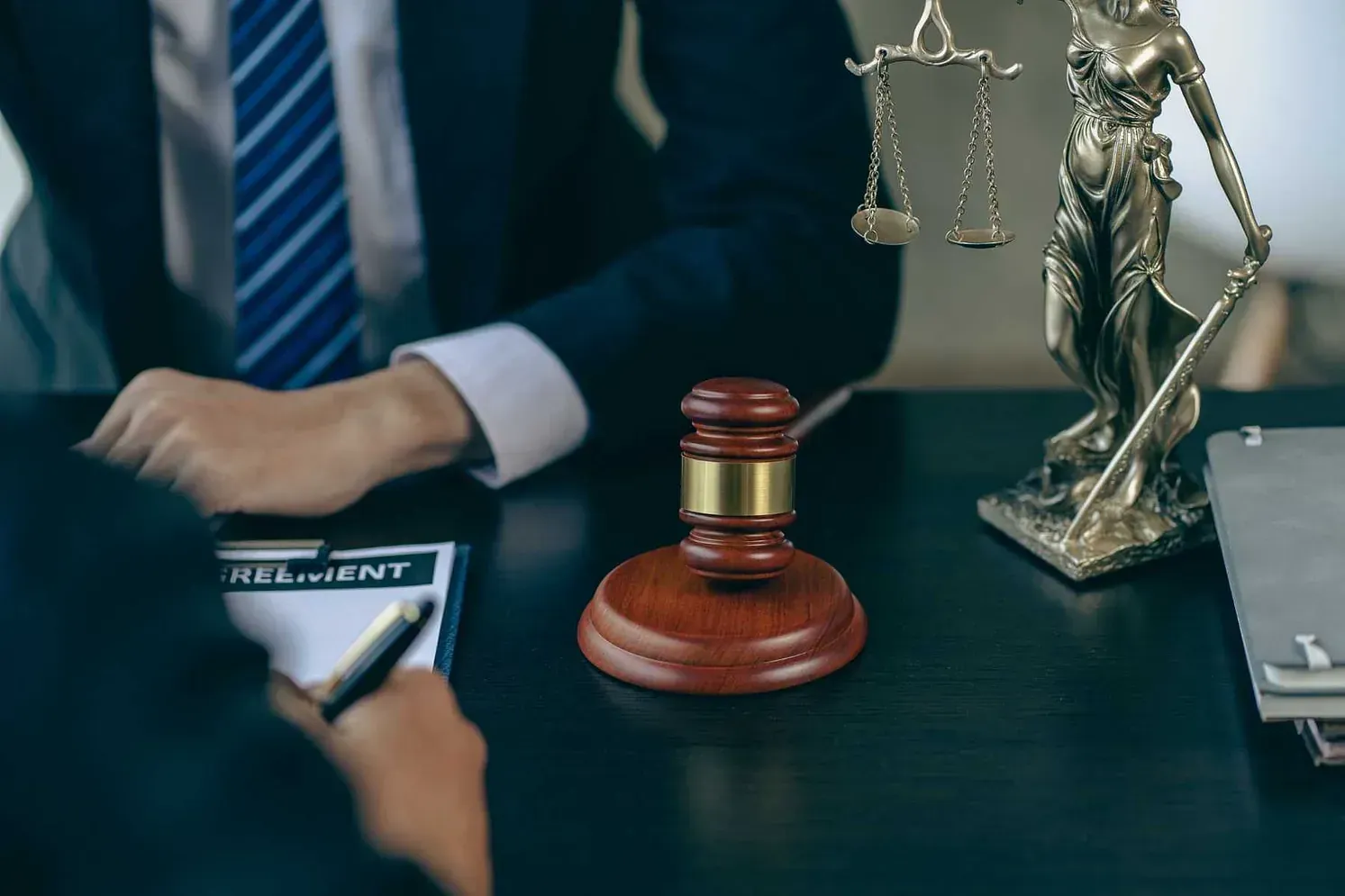 Un hombre con traje y corbata está sentado en una mesa con un mazo y una estatua de la justicia.