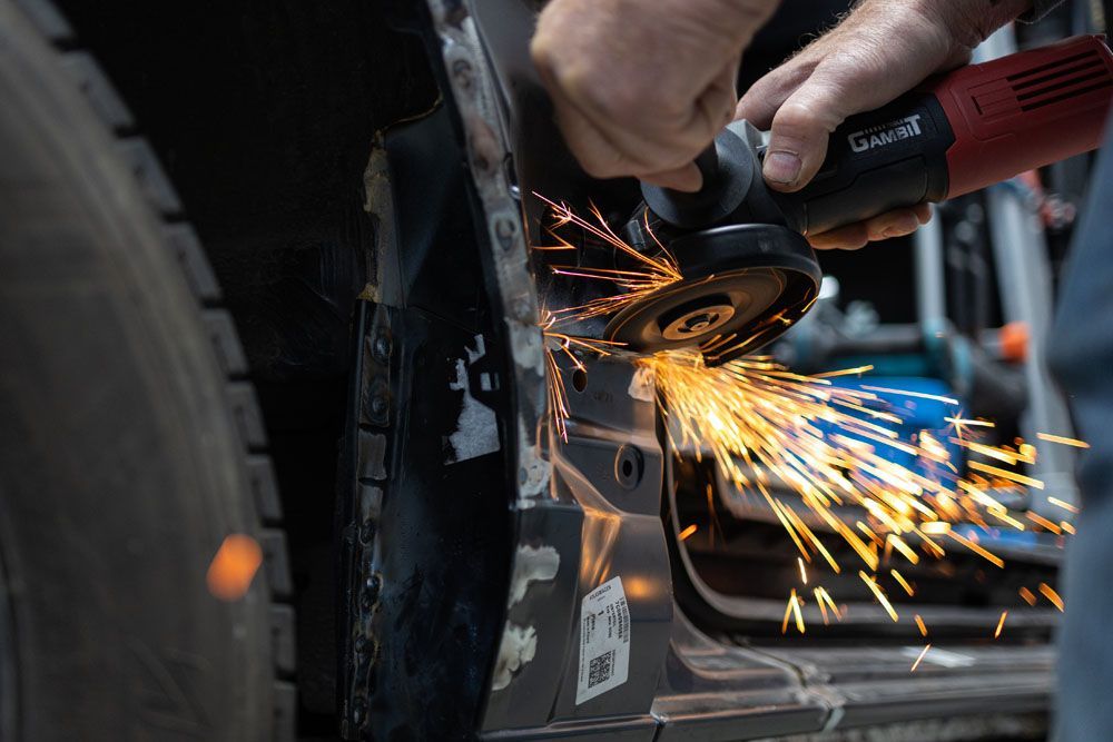 Eine Person schleift mit einer Schleifmaschine ein Metallstück an einem Auto.