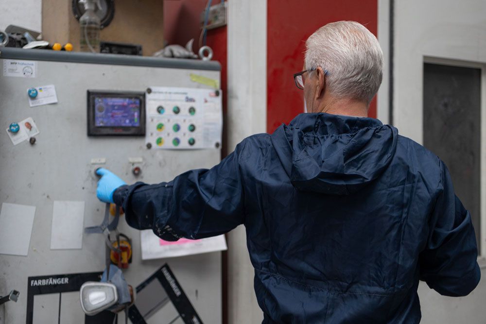 Ein Mann in einer blauen Jacke steht vor einer Maschine.