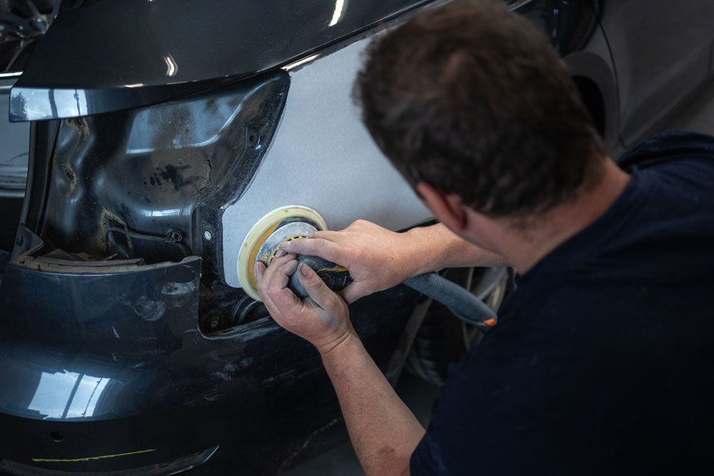 Ein Mann poliert die Seite eines Autos mit einer Schleifmaschine.