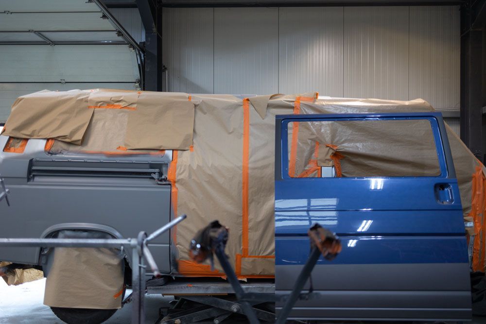 Ein blauer Lieferwagen wird in einer Garage lackiert.