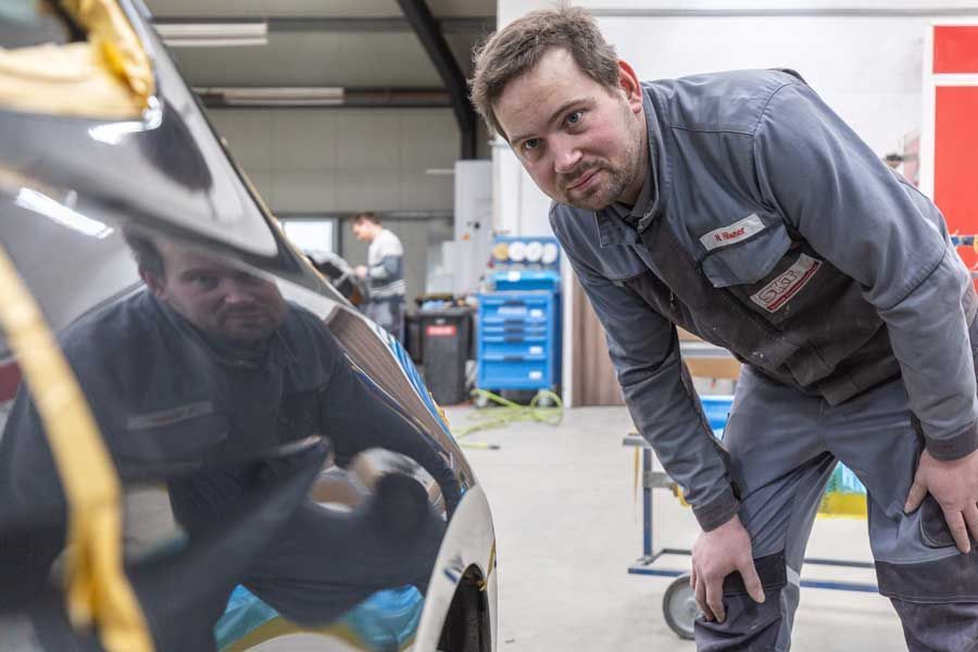 Ein Mann steht neben einem Auto in einer Garage.