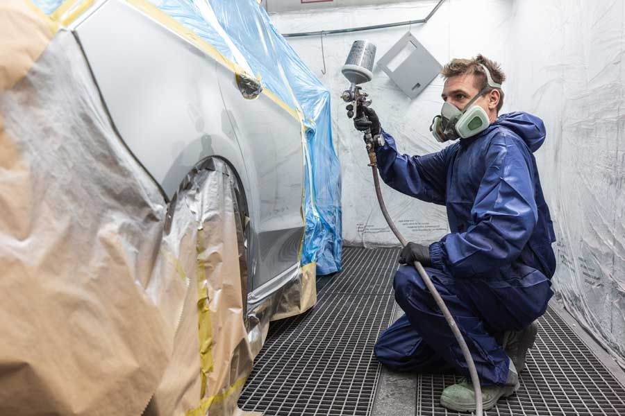 Ein Mann bemalt in einer Lackierkabine ein Auto mit Sprühfarbe.