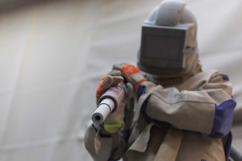 Ein Mann mit Helm und Handschuhen sandstrahlt eine Wand.
