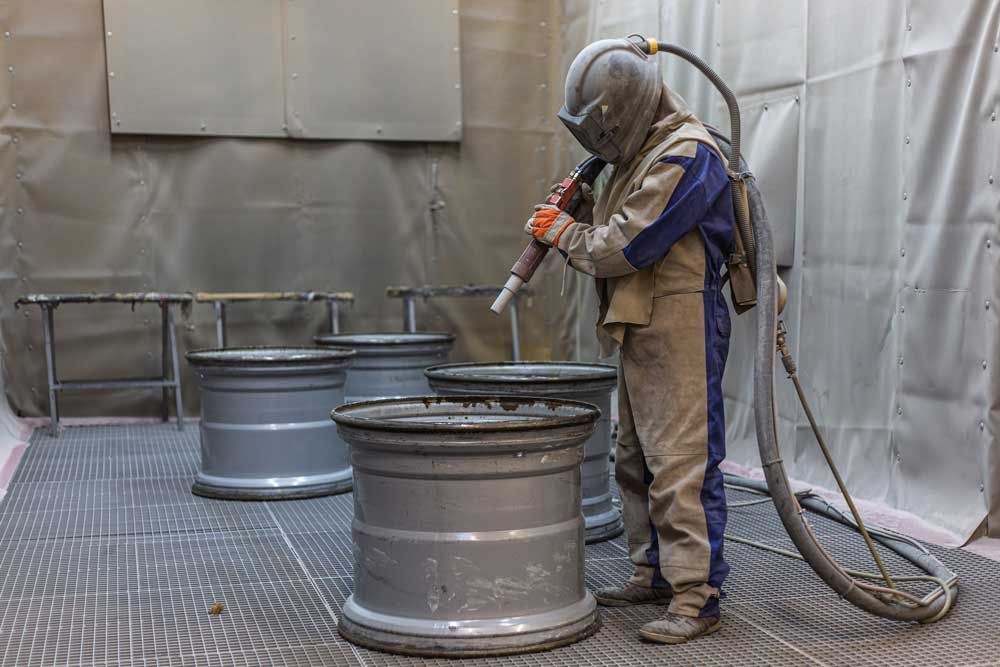 Ein Mann sandstrahlt Räder in einem Raum.