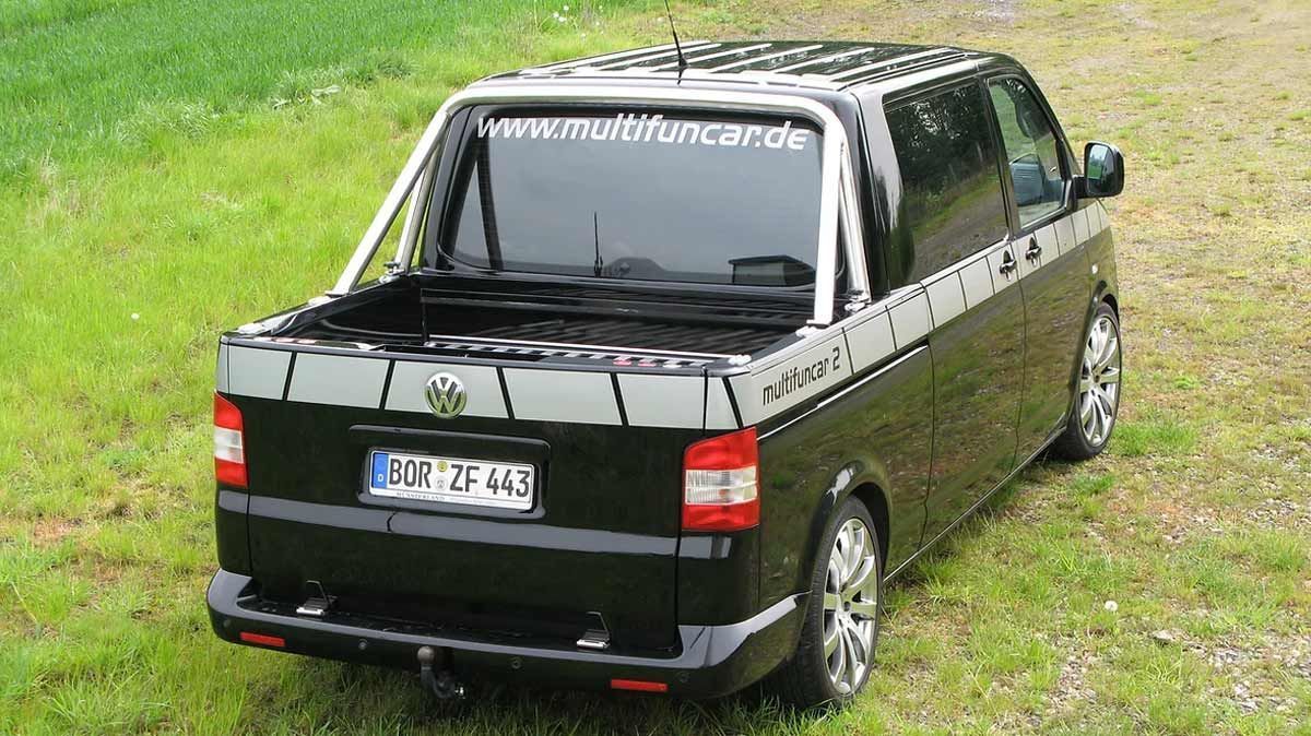 Ein schwarzer Lieferwagen mit Dachgepäckträger ist auf einer Wiese geparkt.