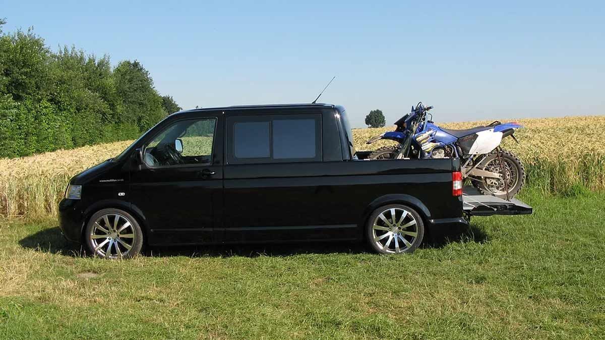 Ein schwarzer Lieferwagen mit einem Motorrad auf der Ladefläche ist auf einer Wiese geparkt.